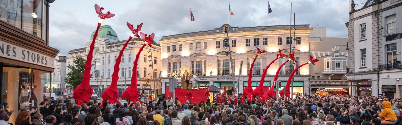 Les Girafes, tall red giraffe sculptures tower over a large crowd of people